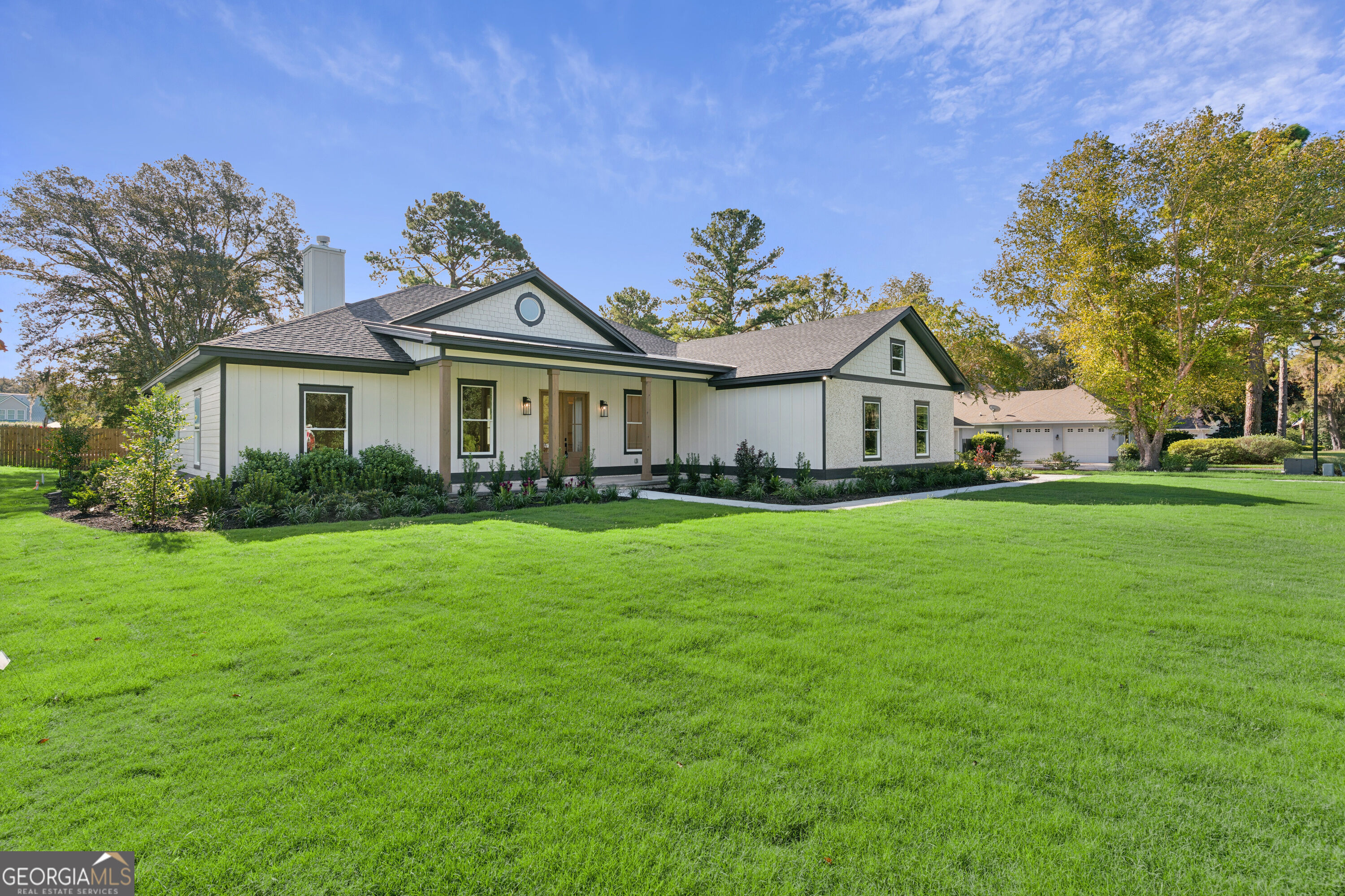 Single-story white home with a covered porch and attached garage behind a broad green lawn.