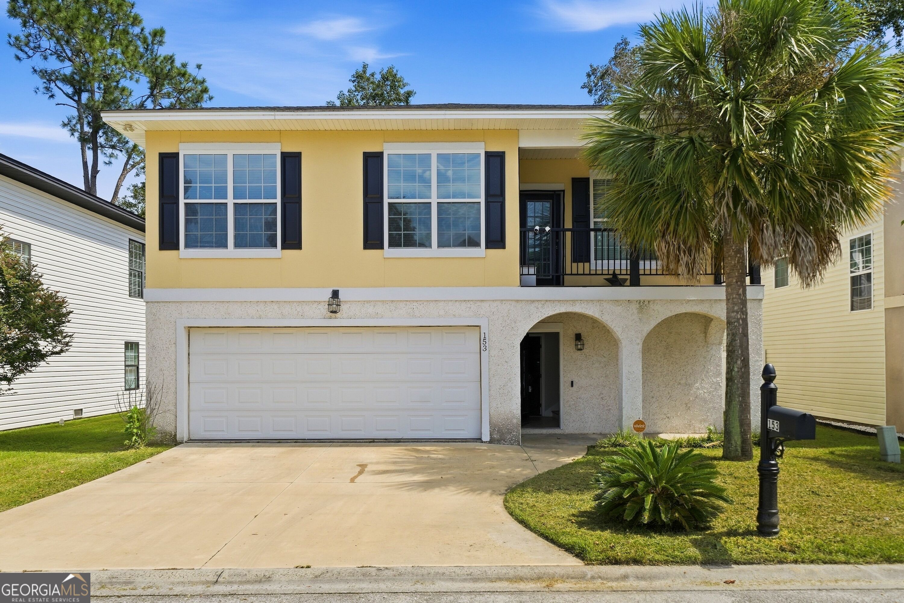Yellow two-story home with a double garage, arched entry, and palm tree.