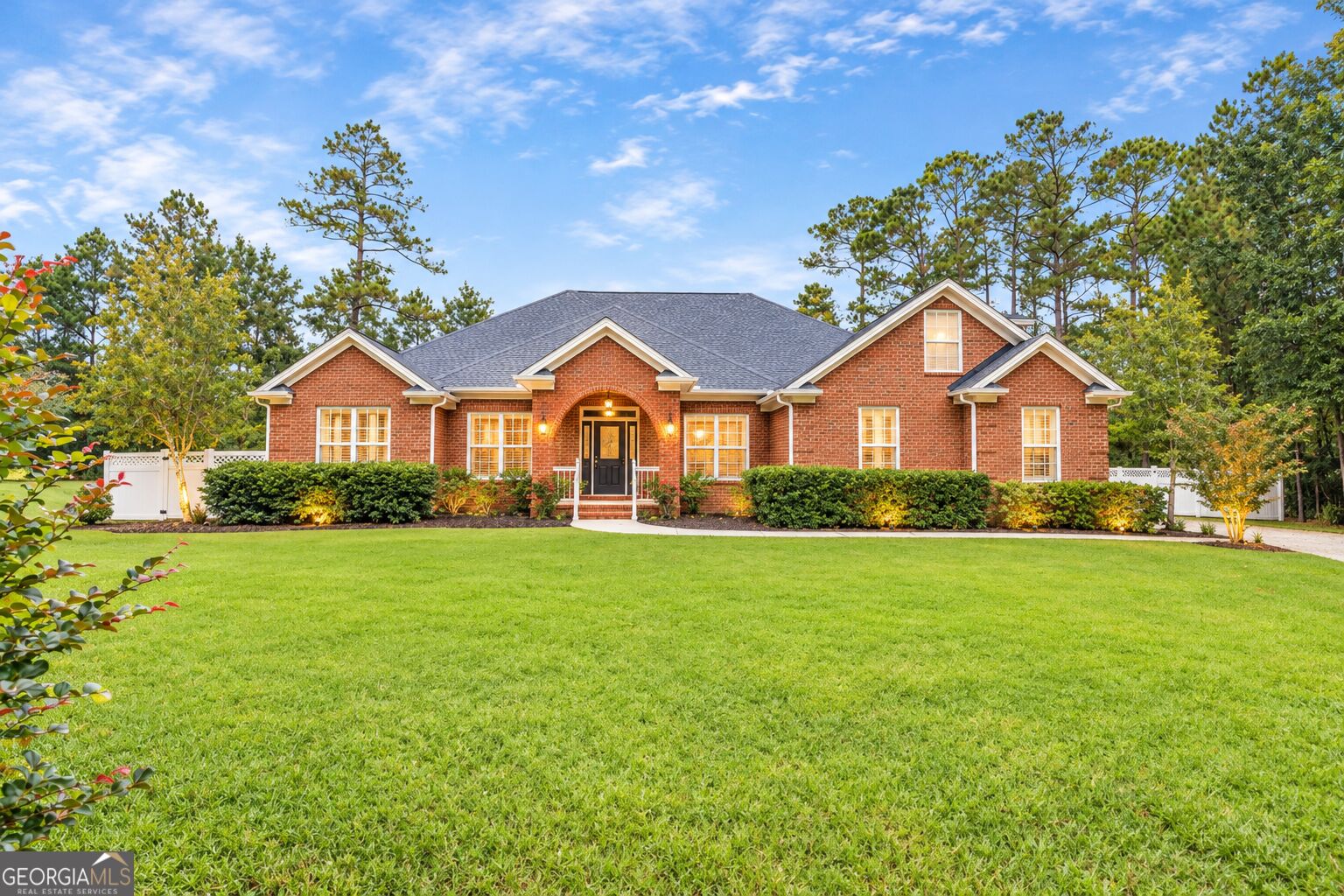 Red brick home with an arched entrance, landscaped shrubs, and a broad green lawn.