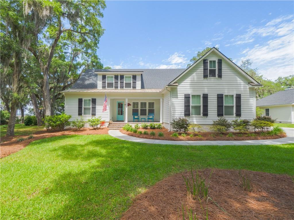 Light-colored two-story home with dark shutters, teal front door, and a covered porch beneath mature trees.
