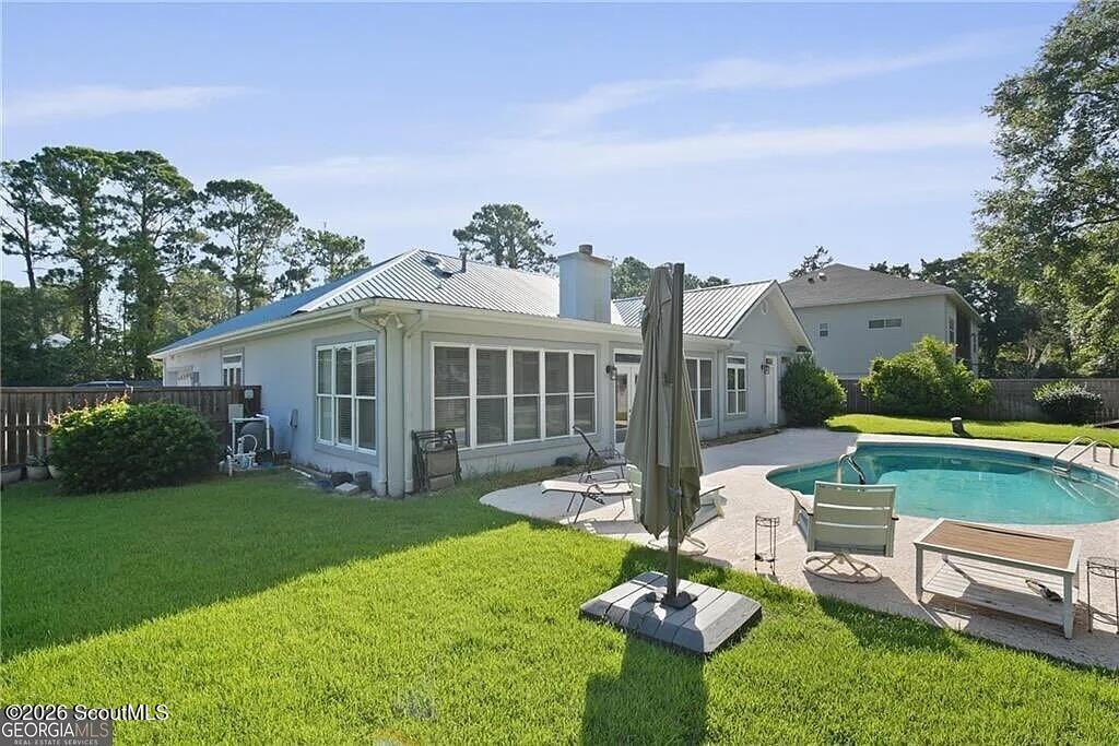 Home’s rear exterior with a swimming pool, patio furniture, and broad green lawn.