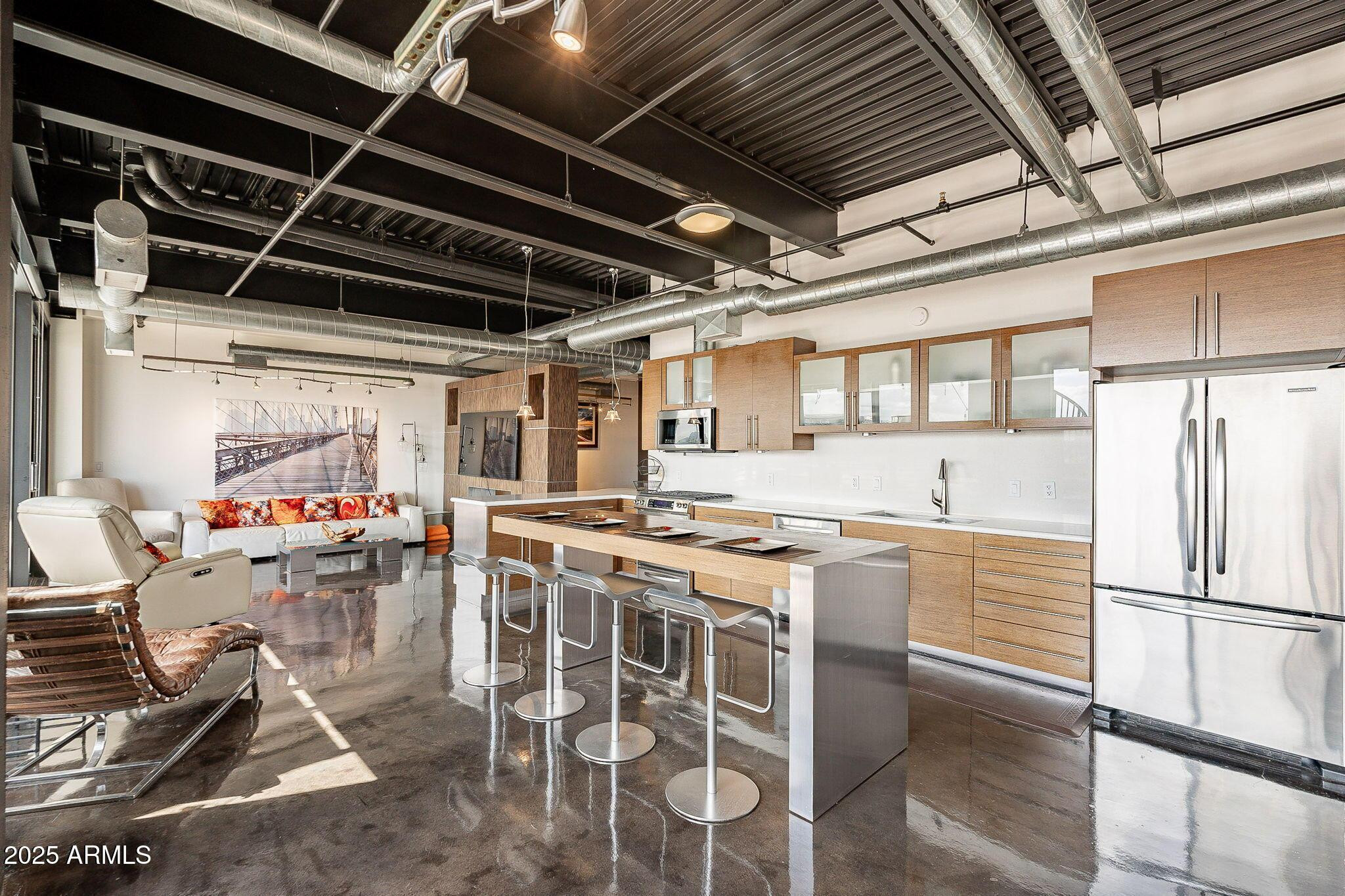 Open-plan loft kitchen with a large island, stainless appliances, exposed ducts, and polished concrete floors.