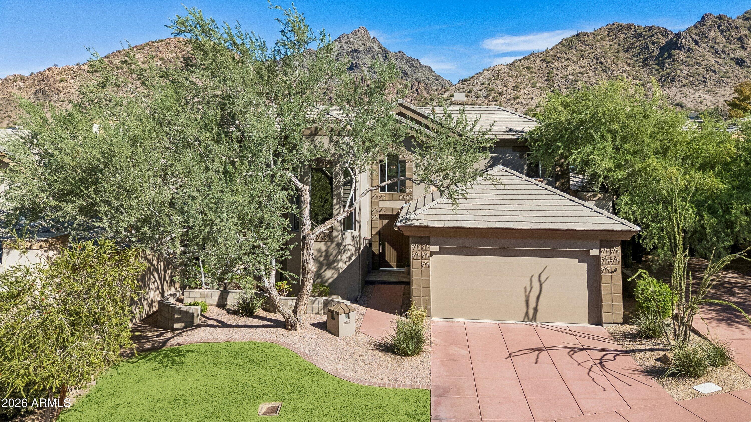 Tan stucco home with a two-car garage, desert landscaping, and rocky mountains behind it.
