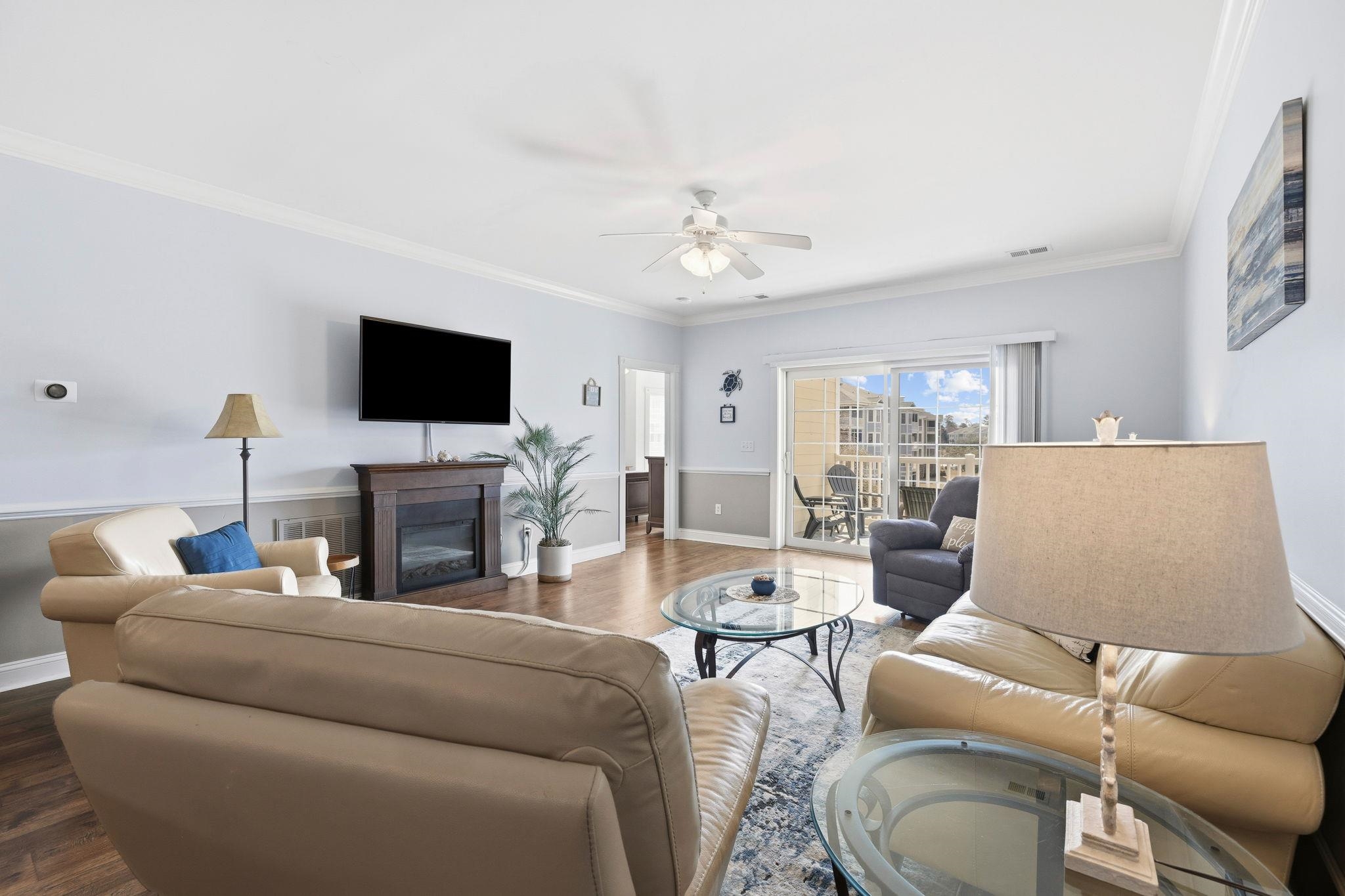 Furnished condo living room with beige leather sofas, fireplace, and sliding doors to a balcony.