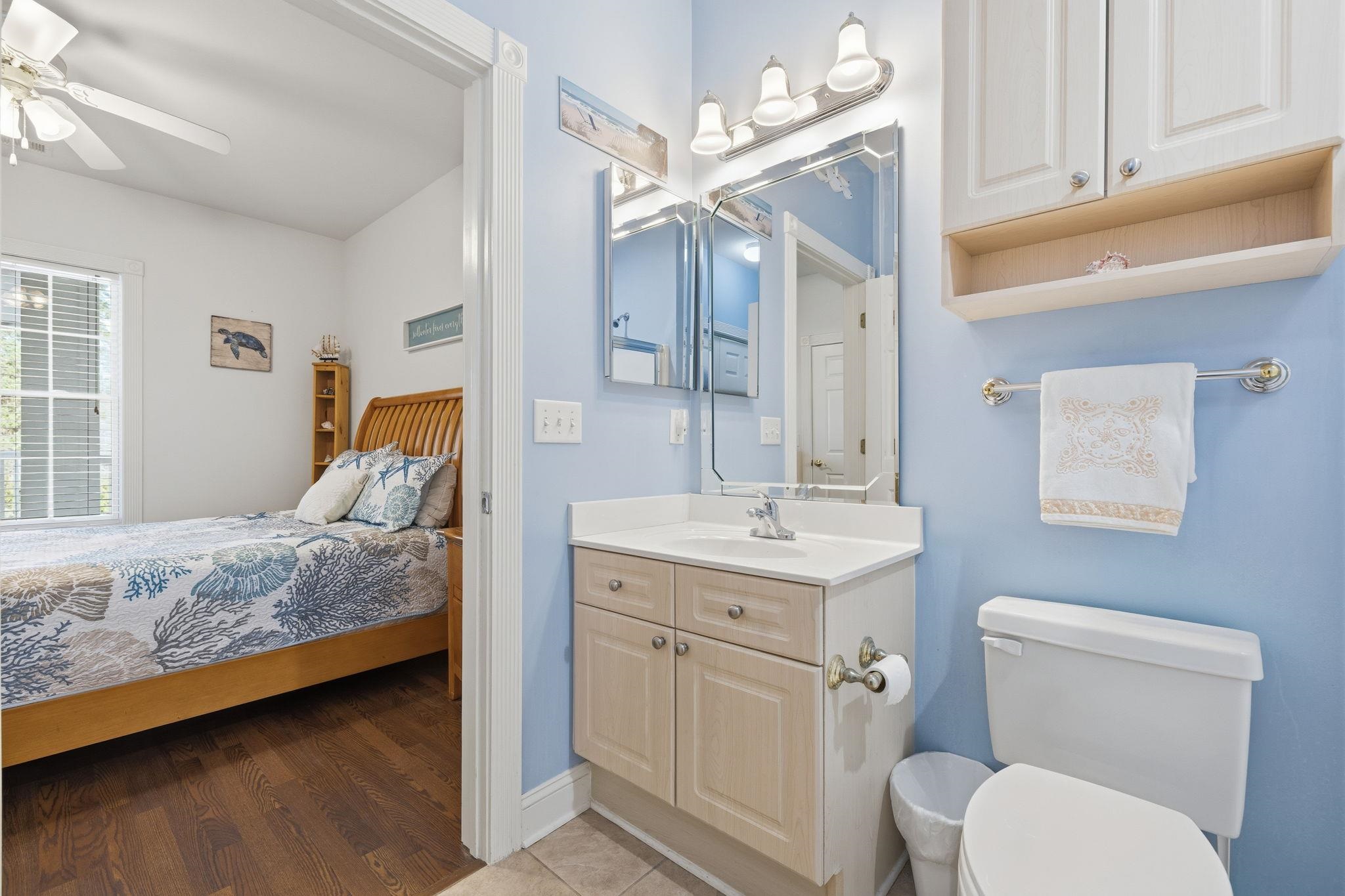 Bathroom vanity and toilet beside a bedroom with a wooden bed and patterned coastal bedding.