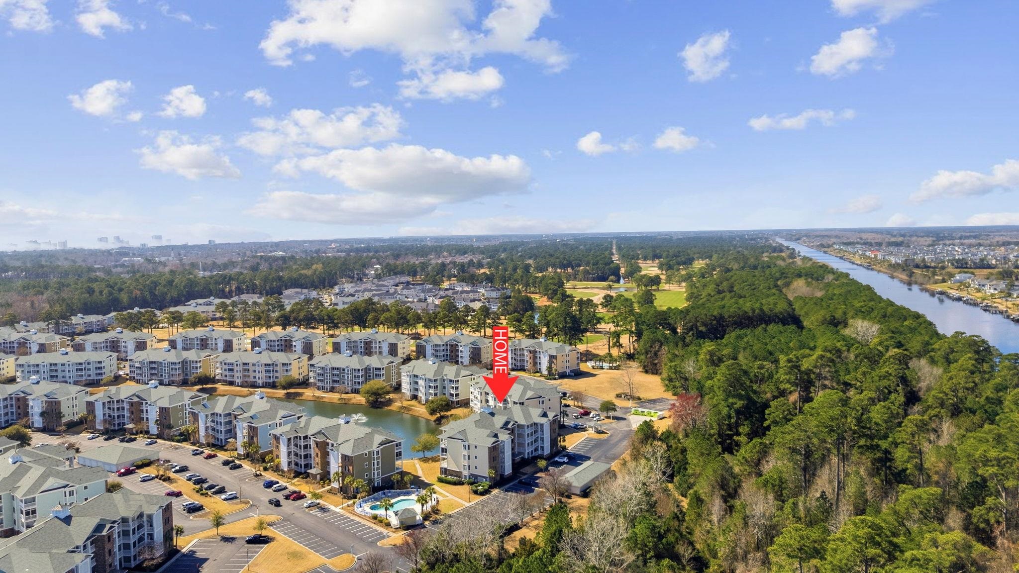 Aerial view of condominium buildings beside a canal, with the unit marked by a red arrow.
