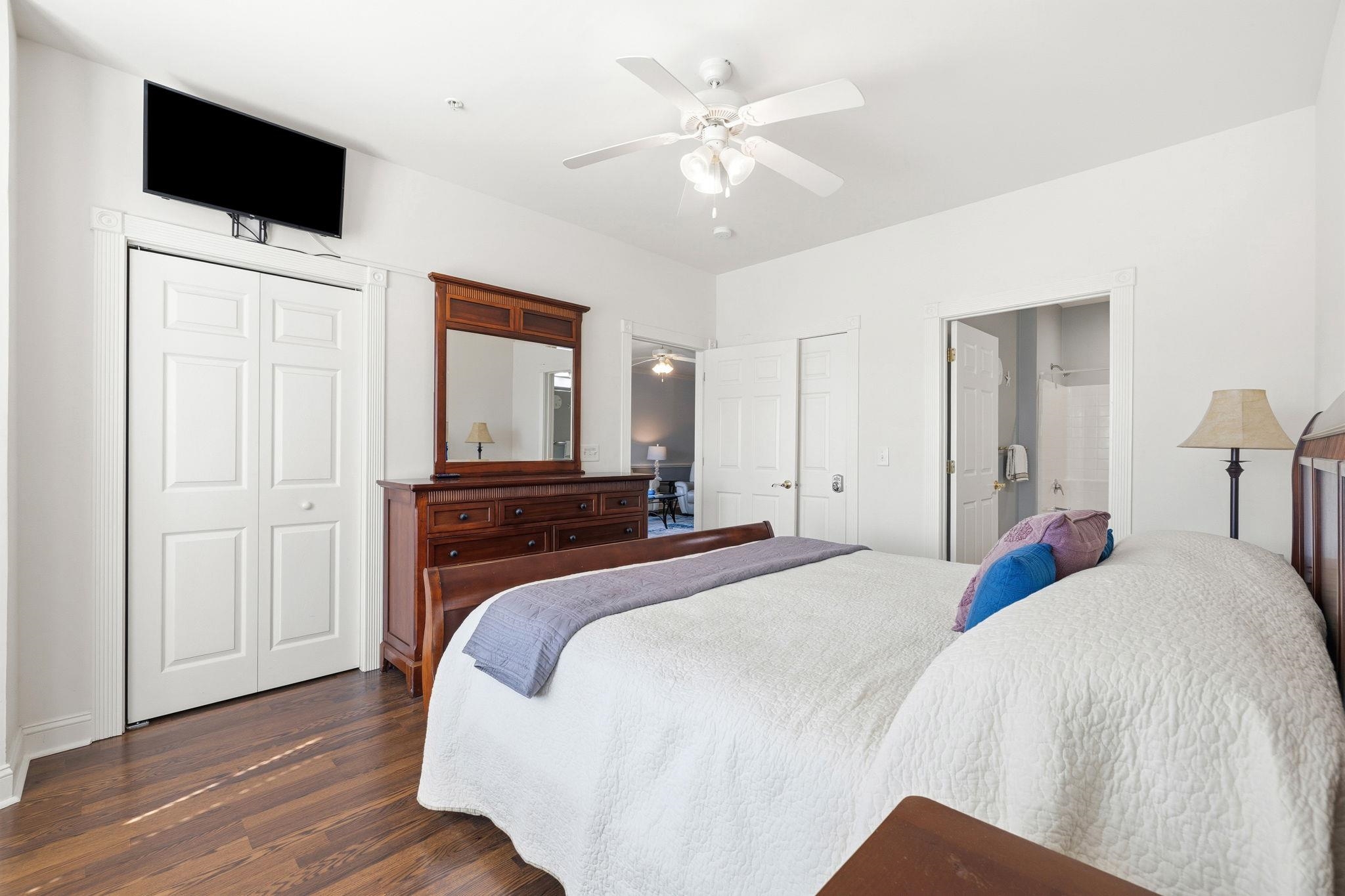 Bedroom with a white-covered bed, dark wood dresser and mirror, and hardwood floors.