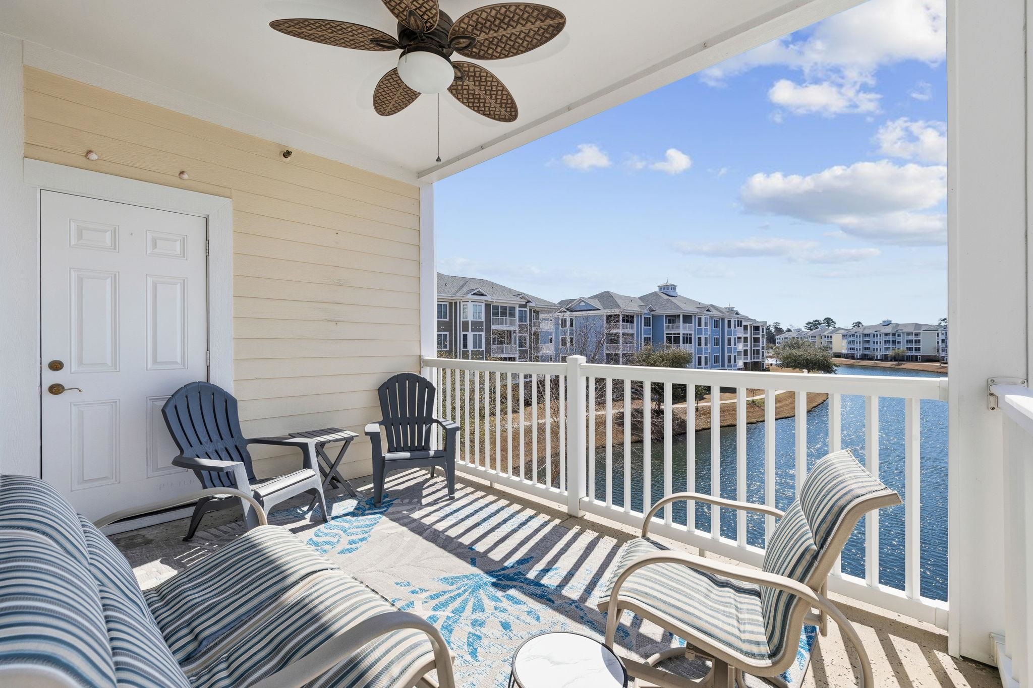 Covered balcony overlooking a pond, furnished with striped lounge chairs and Adirondack chairs.