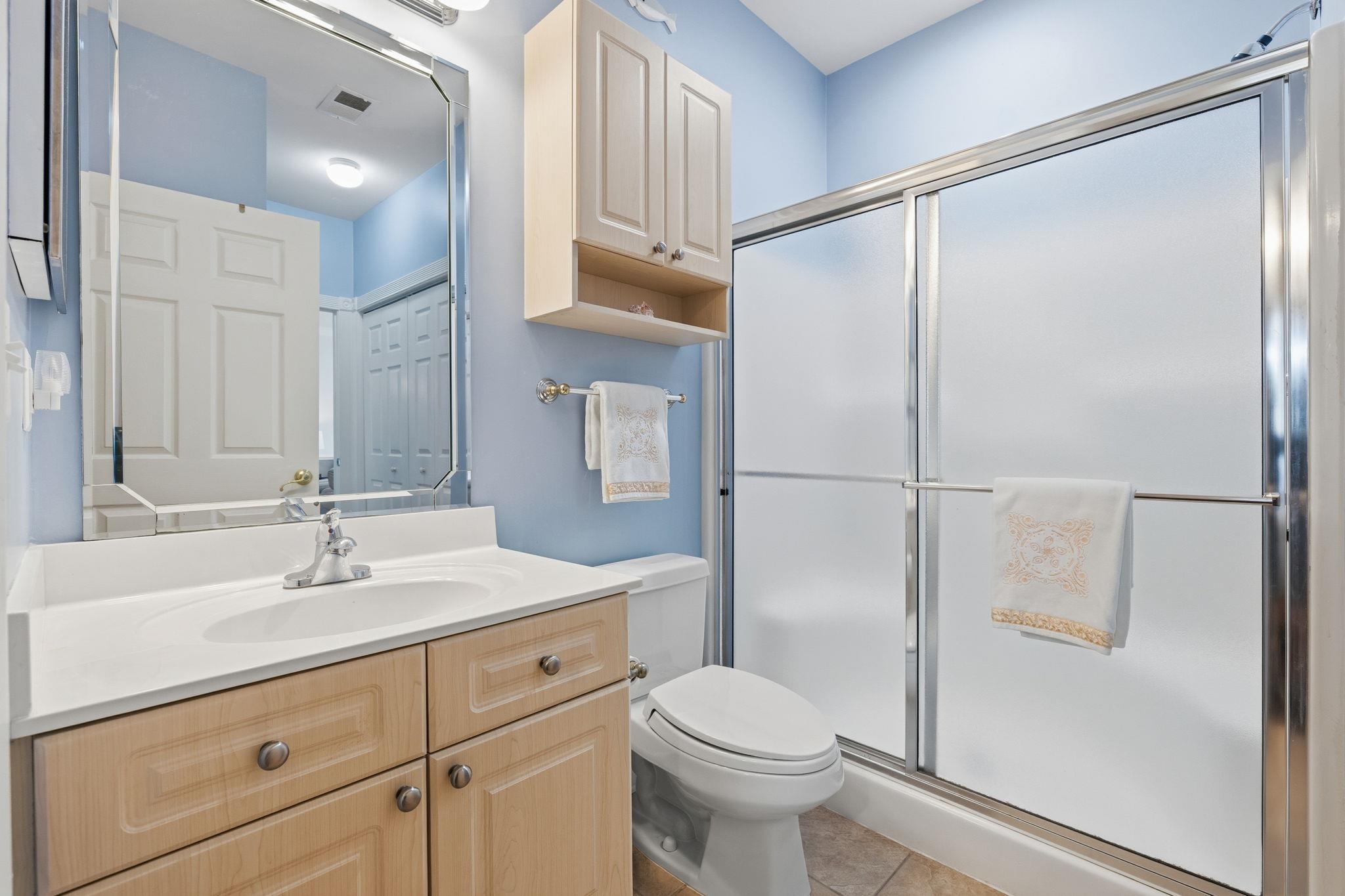Bathroom with a light wood vanity, blue walls, and a frosted-glass shower.