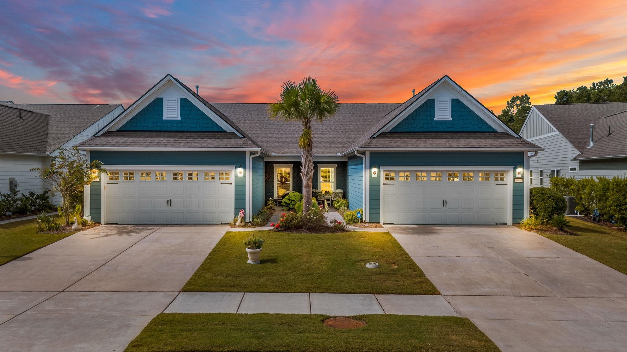 Teal-sided home with twin white garage doors and a central palm tree at sunset.