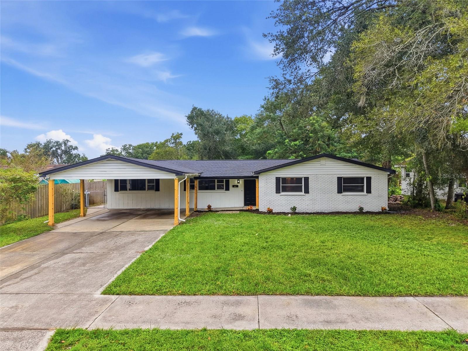 Single-story white home with a covered carport, concrete driveway, and broad green lawn.