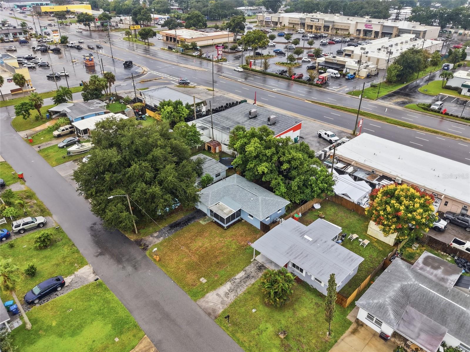 Aerial view of a blue-gray house with a fenced yard near a busy commercial intersection.