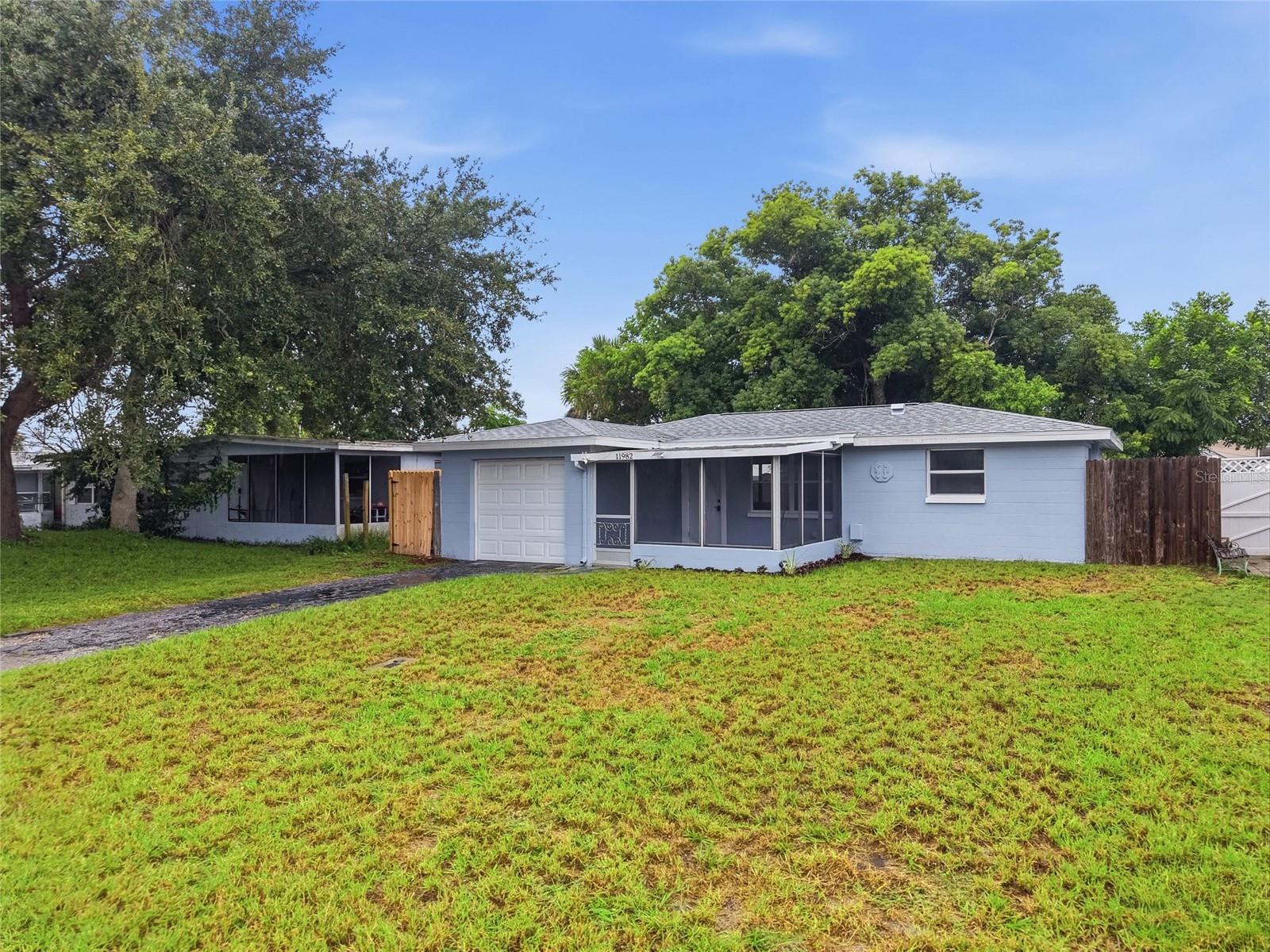 Blue single-story home with a screened porch, attached garage, and grassy front yard.
