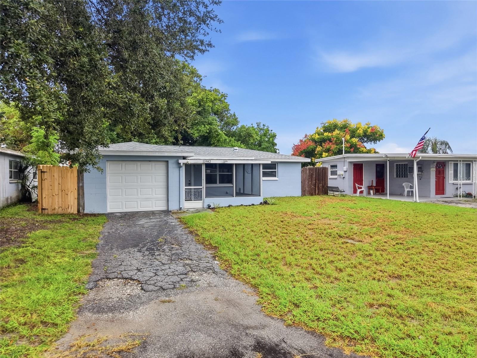 Single-story blue house with attached garage, screened entry porch, and cracked driveway.