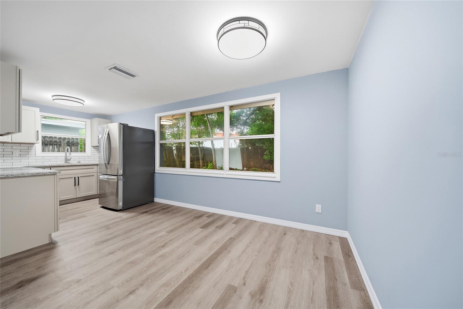 Vacant kitchen and dining area with pale wood-look floors, blue walls, and large windows.