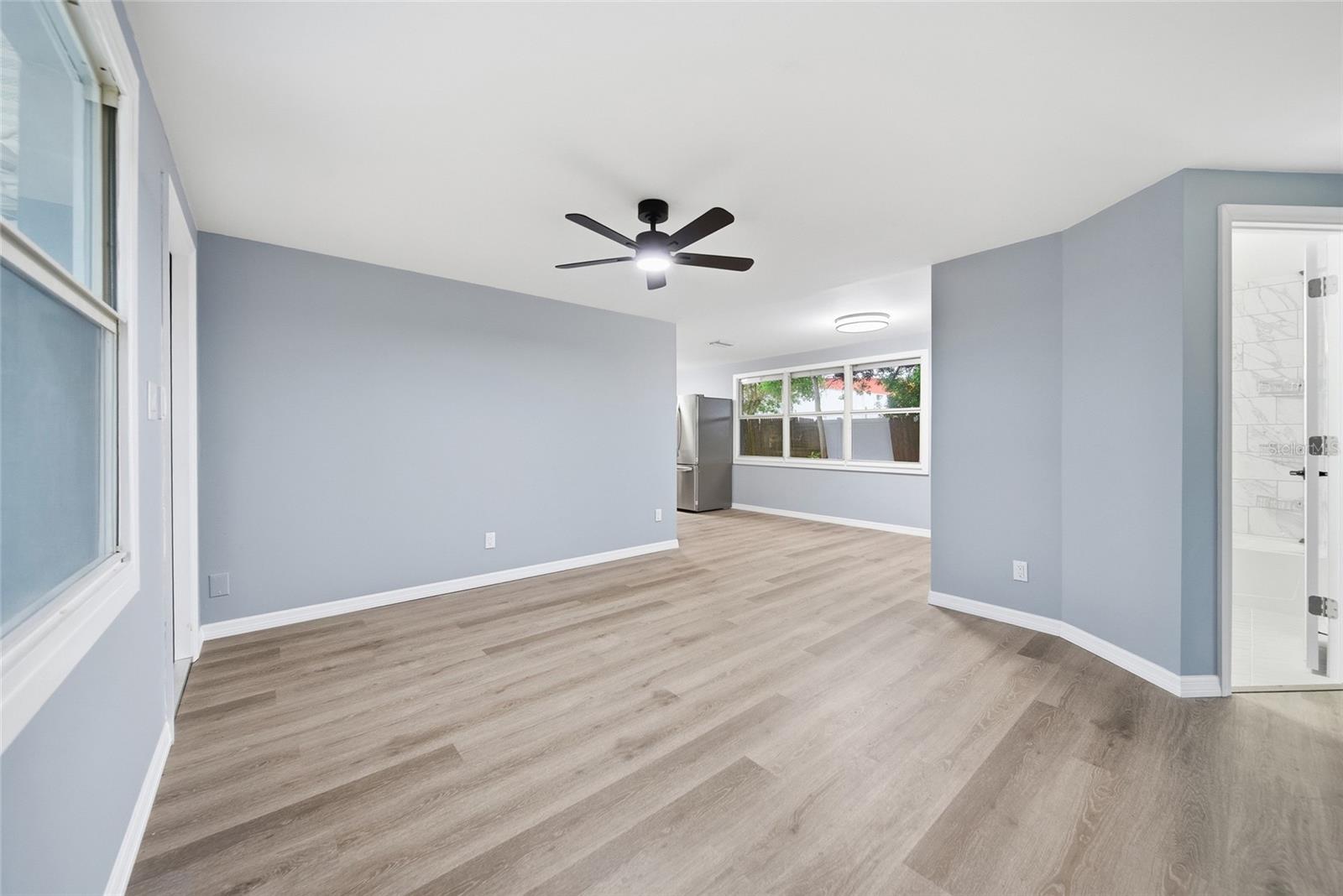 Vacant living area with light wood-look floors, pale blue-gray walls, and a black ceiling fan.