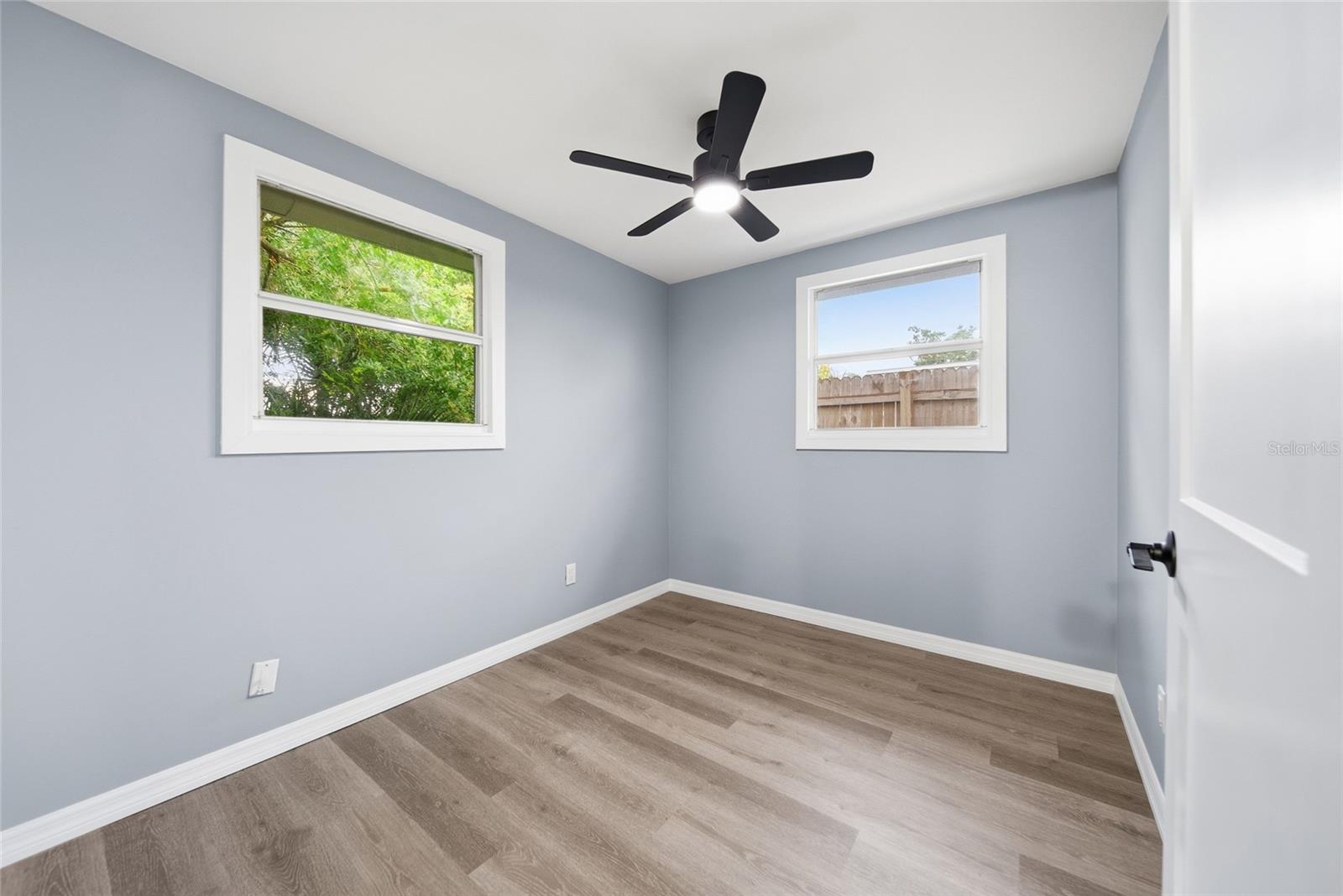 Vacant bedroom with wood-look floors, two windows, and a black ceiling fan.