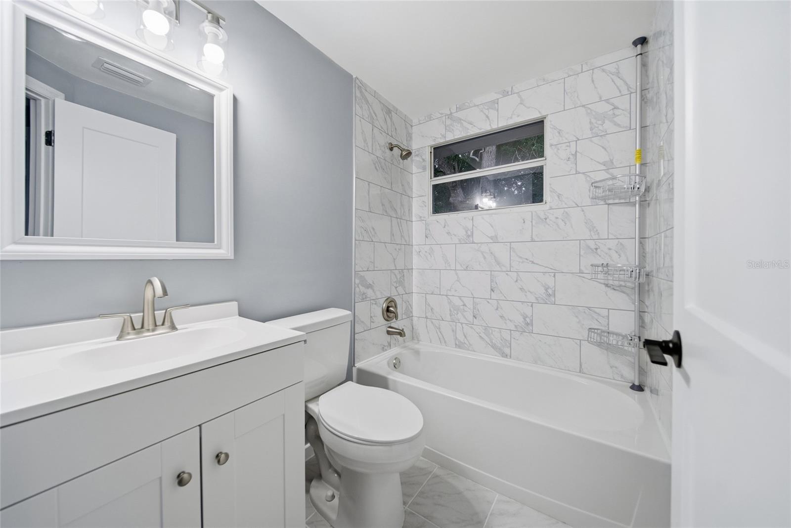 Bathroom with a white vanity, toilet, and tub lined with marble-look tile.