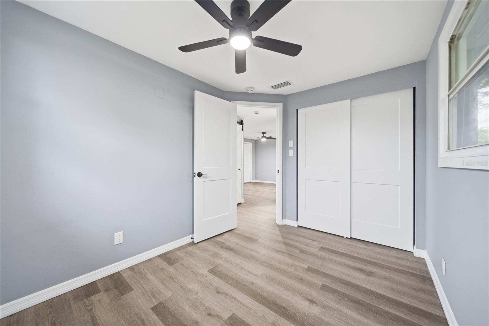 Empty bedroom with wood-look floors, a ceiling fan, and white sliding closet doors.