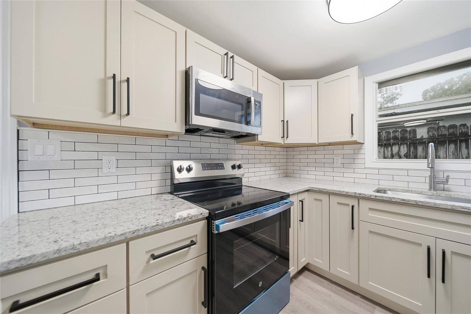 Renovated kitchen with cream cabinets, stone counters, subway-tile backsplash, and stainless appliances.