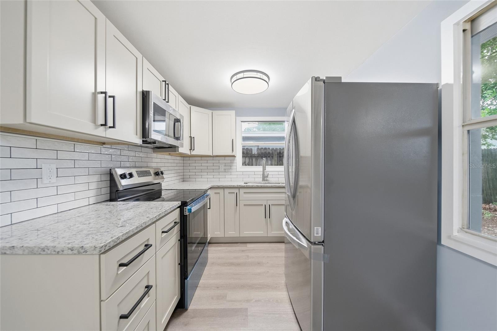 Renovated kitchen with white cabinets, granite counters, subway-tile backsplash, and stainless steel appliances.