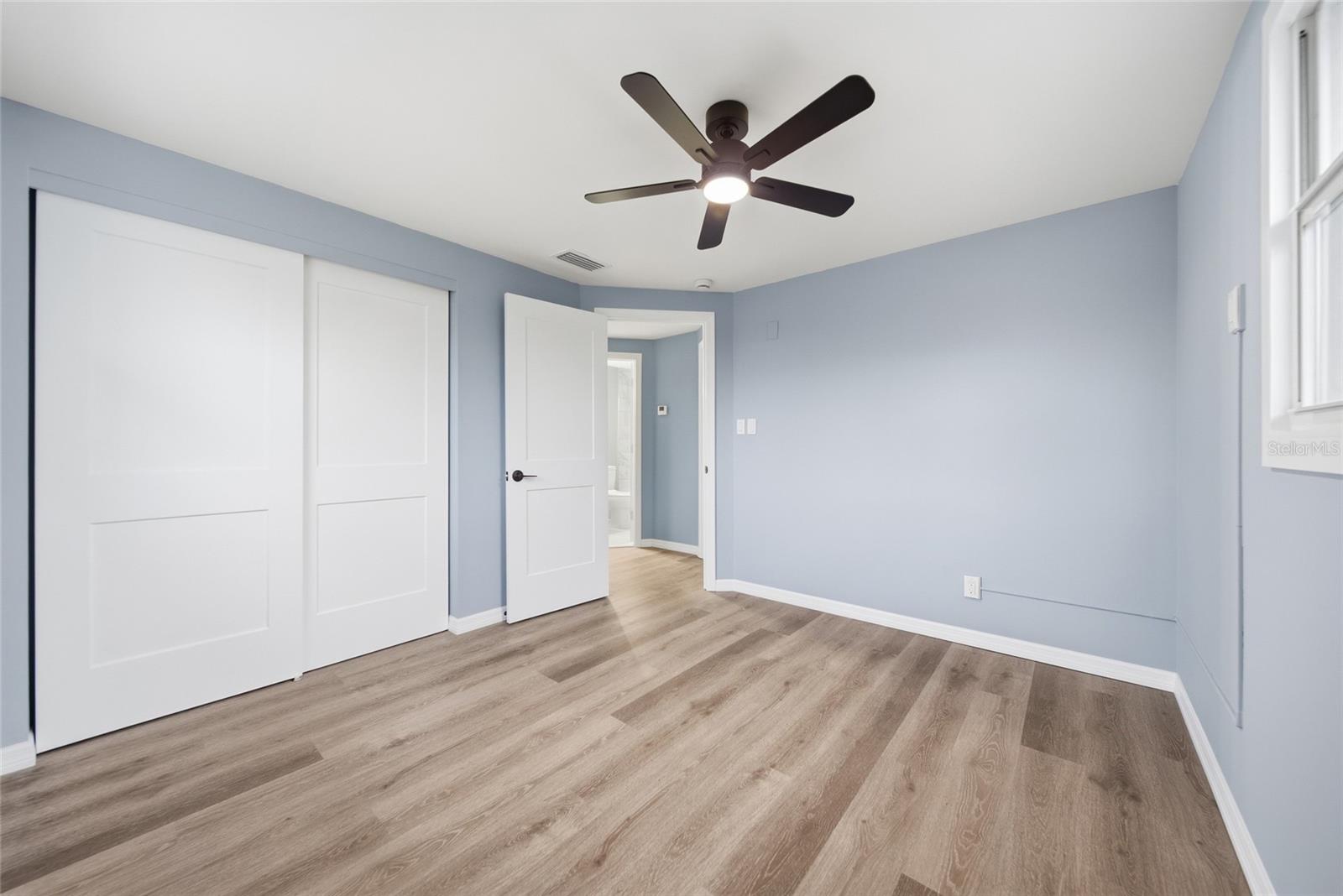 Vacant bedroom with blue walls, wood-look flooring, sliding closet doors, and a dark ceiling fan.
