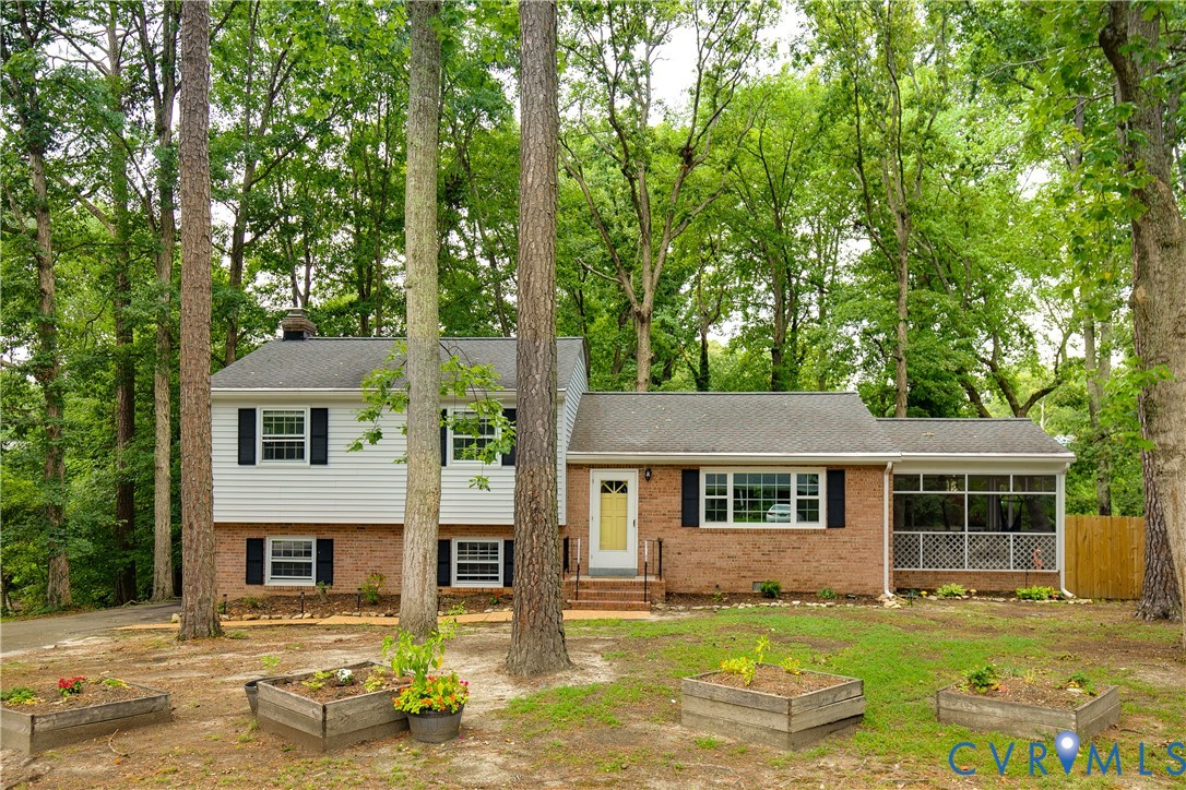 Split-level home with brick and white siding, a yellow front door, screened porch, and wooded yard.
