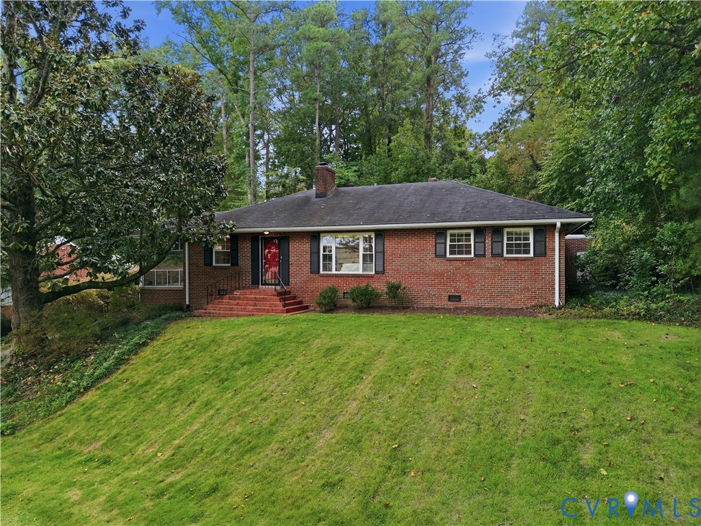 Red brick ranch house with black shutters and a red front door, set among mature trees.