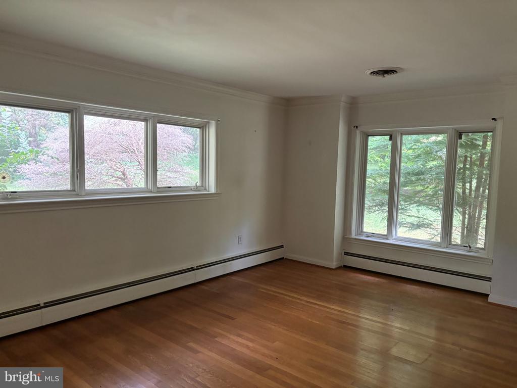 Empty room with hardwood floors and large windows overlooking flowering trees.