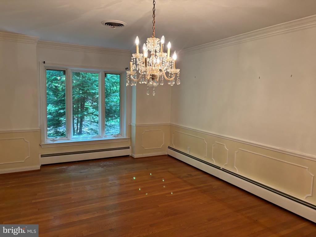 Empty dining room with hardwood floors, paneled walls, a crystal chandelier, and large windows.