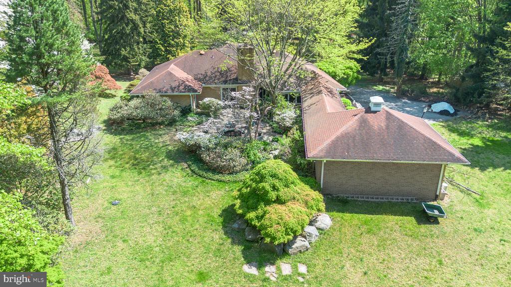 Aerial view of a brick home with broad roofs, landscaped yard, and mature trees.