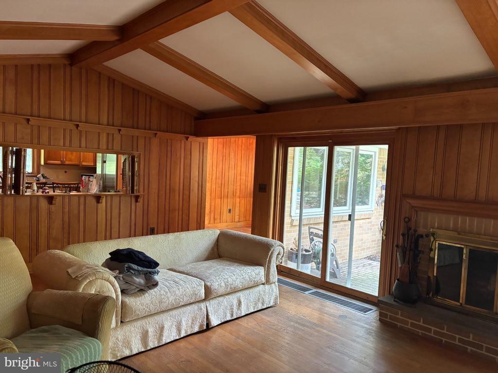 Wood-paneled living room with exposed beams, cream sofas, brick fireplace, and sliding glass doors to a patio.