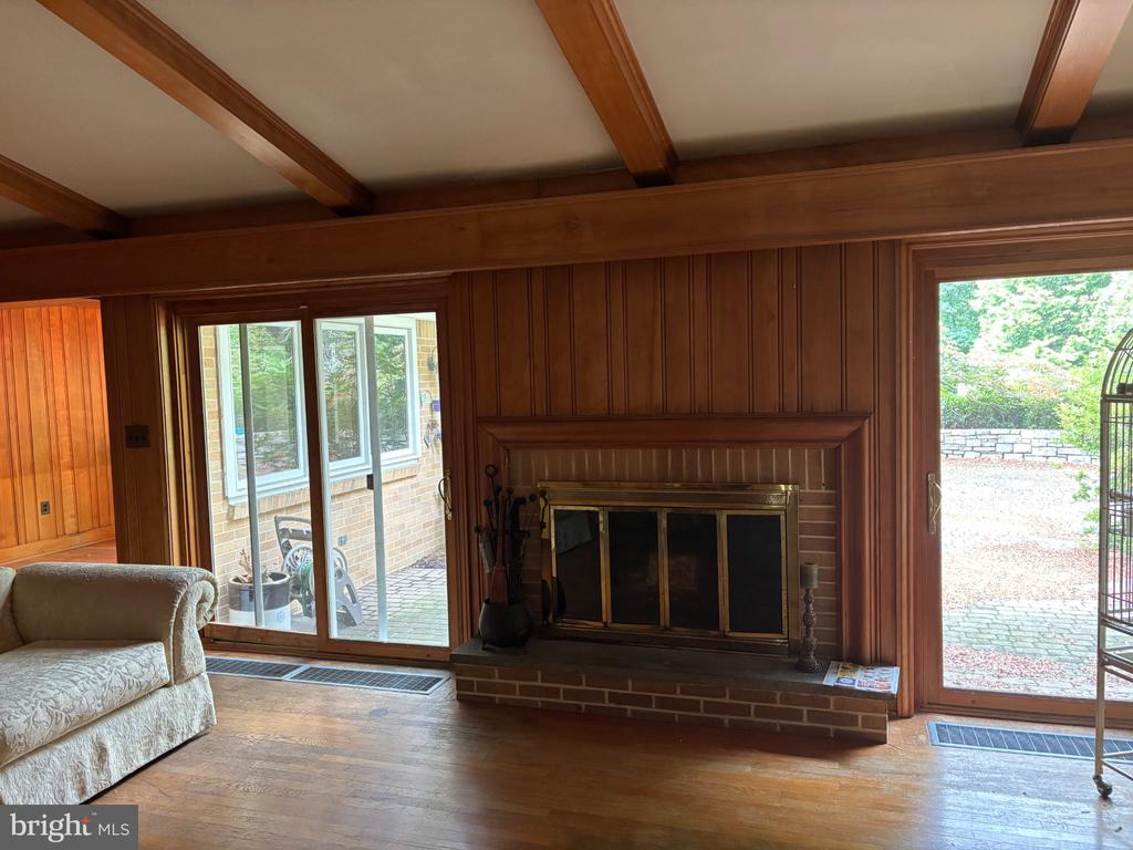 Wood-paneled living room with beamed ceiling, brick fireplace, and sliding glass doors to a patio.