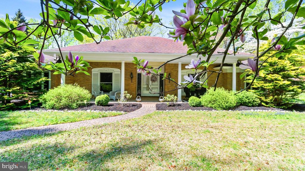 Brick home with a covered porch and curved walkway, framed by flowering magnolia branches.