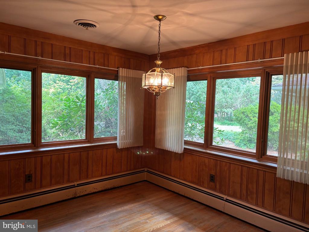Empty wood-paneled room with wraparound windows, hardwood floors, and a chandelier.