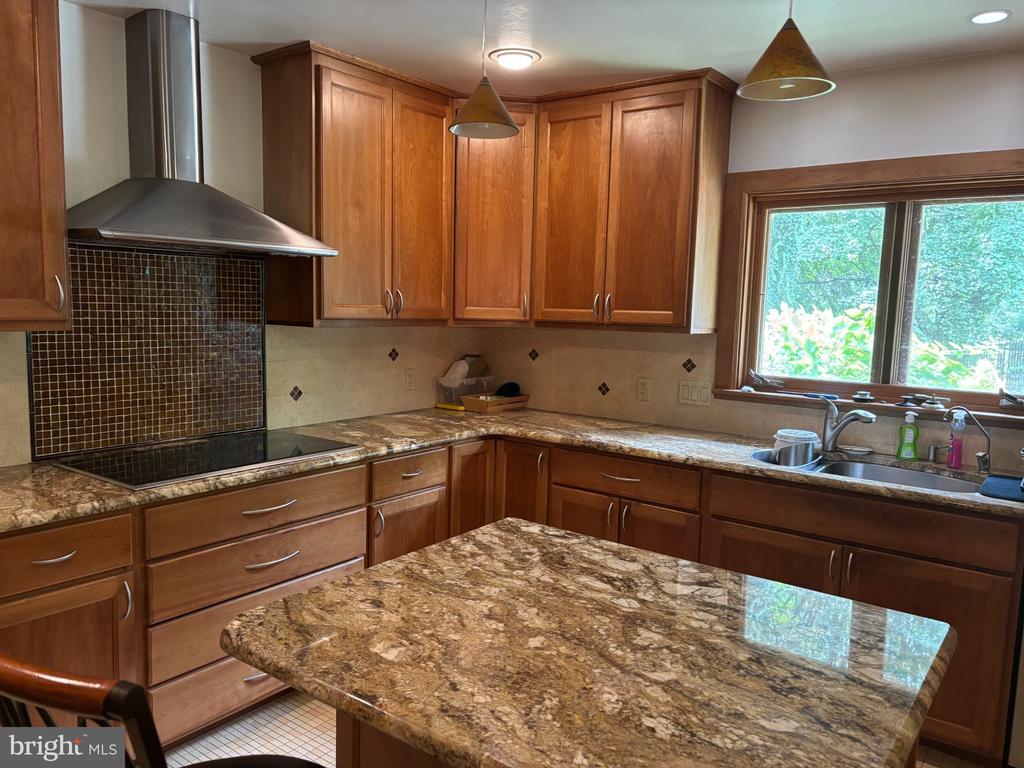 Kitchen with warm wood cabinetry, granite island, and sink beneath a large window.