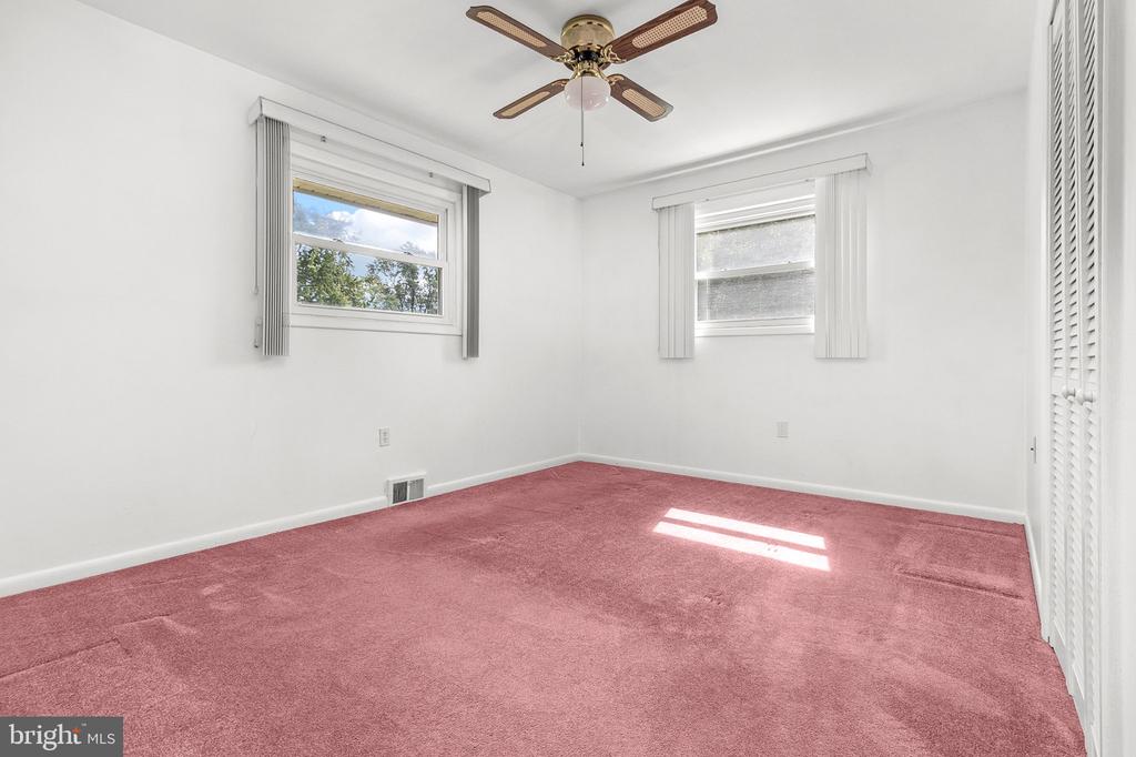 Empty bedroom with pink carpet, two windows, a ceiling fan, and a louvered closet door.