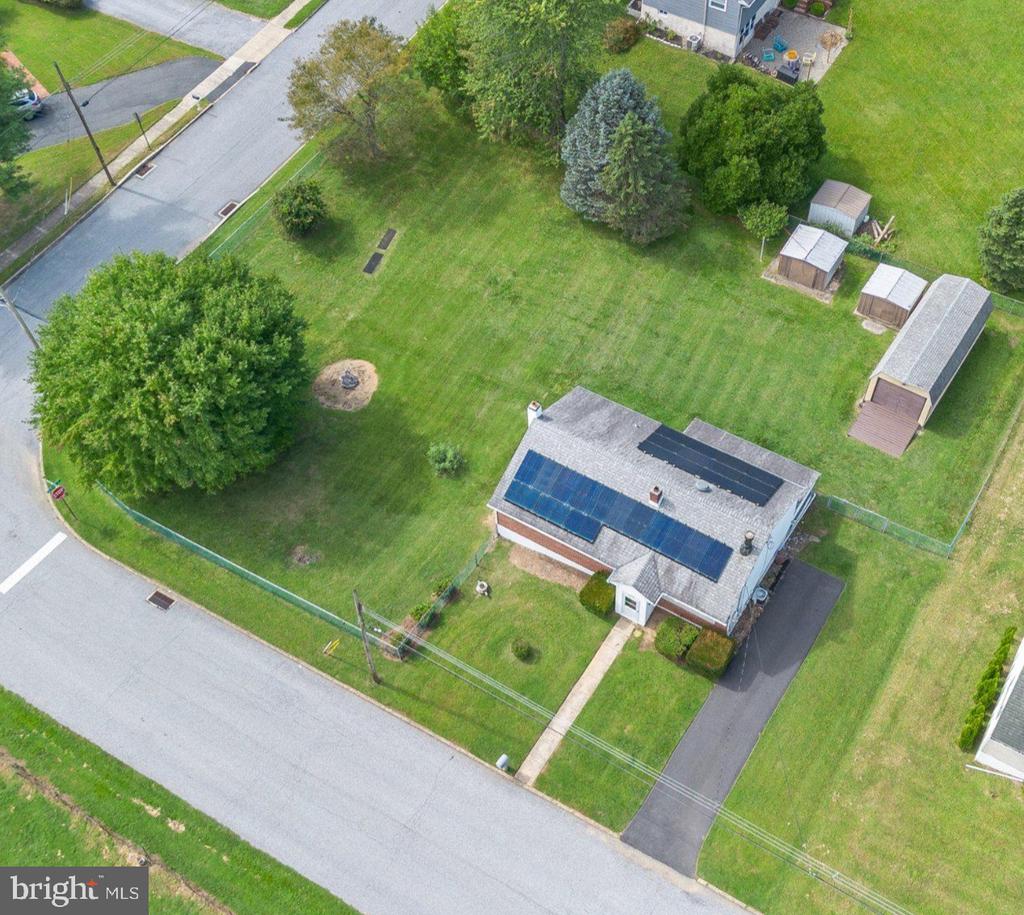 Aerial view of a brick home with solar panels, a fenced lawn, and several sheds.