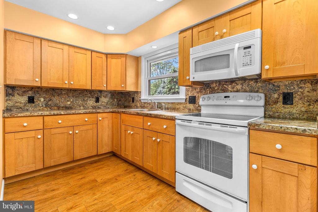 Kitchen with honey-colored wood cabinets, patterned stone counters, white appliances, and a window above the sink.