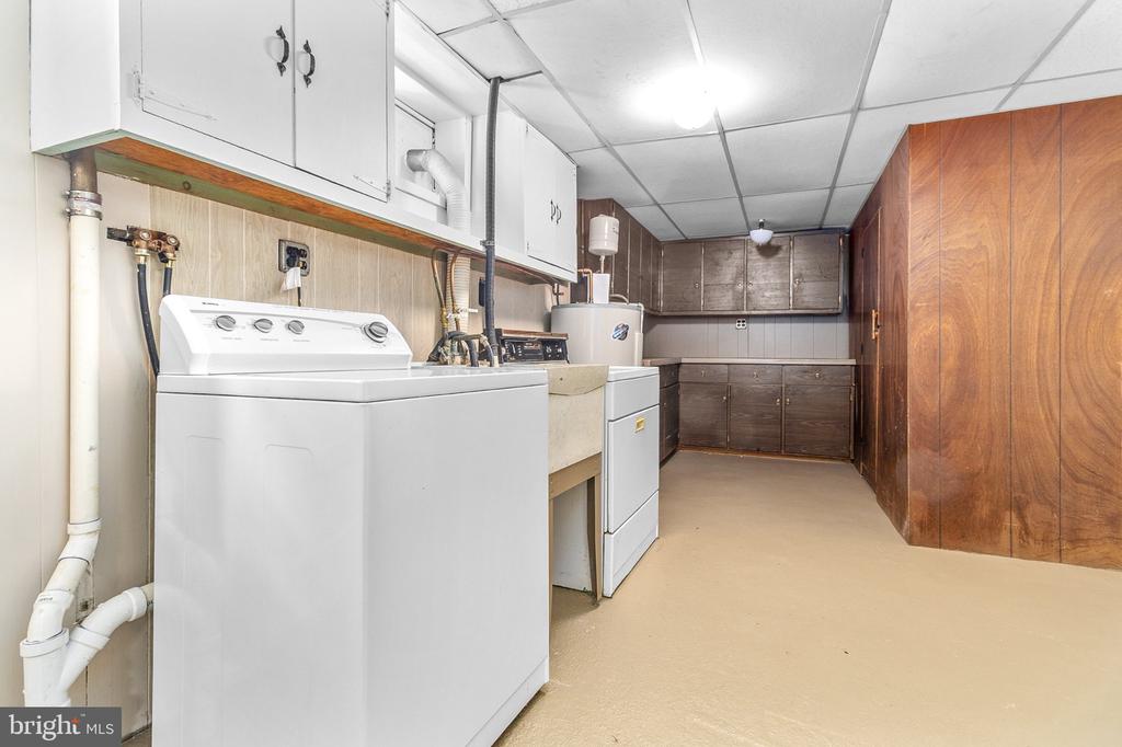 Laundry room with a top-loading washer, dryer, utility sink, and extensive cabinetry.