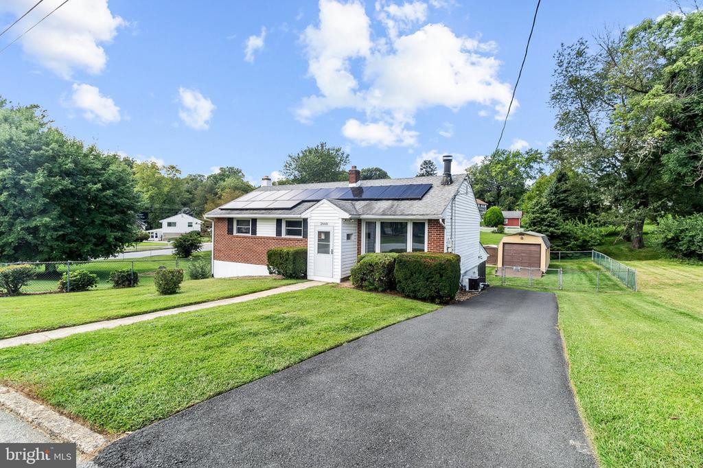 Single-story brick and white-sided home with rooftop solar panels and a wide paved driveway.