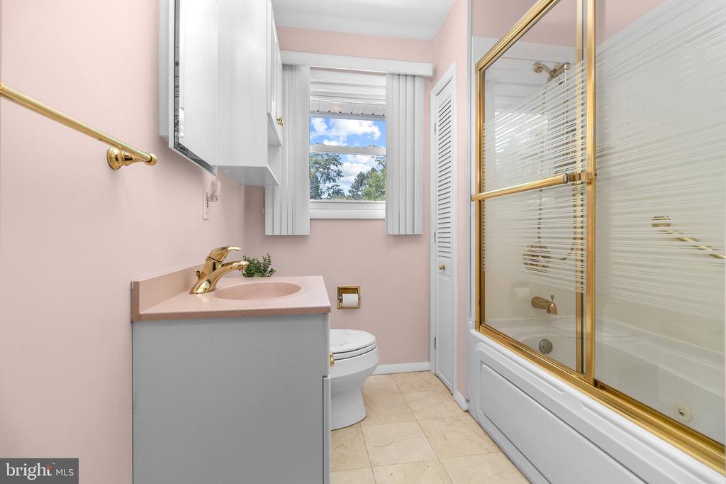 Bathroom with pink walls, a gray vanity, and a white tub-shower enclosure with gold trim.