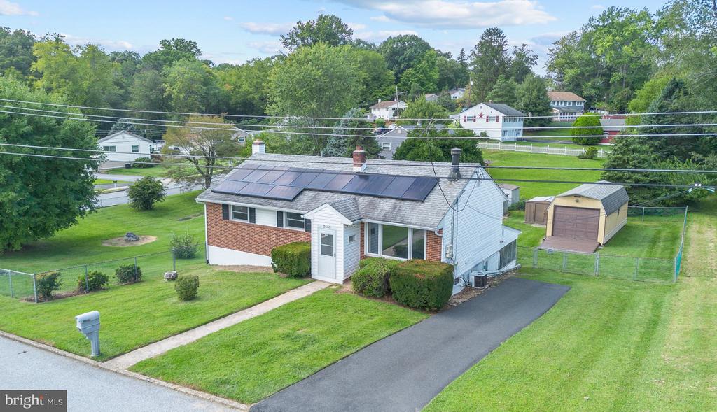 Aerial view of a one-story home with rooftop solar panels, a paved driveway, and a detached shed.