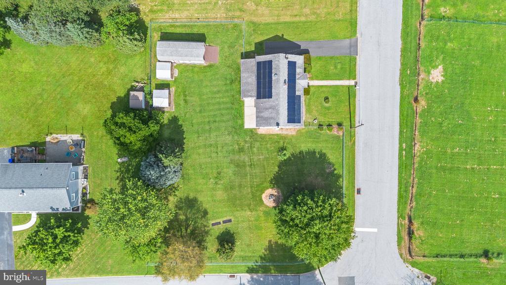 Aerial view of a house with solar panels, outbuildings, and a broad lawn beside a road.