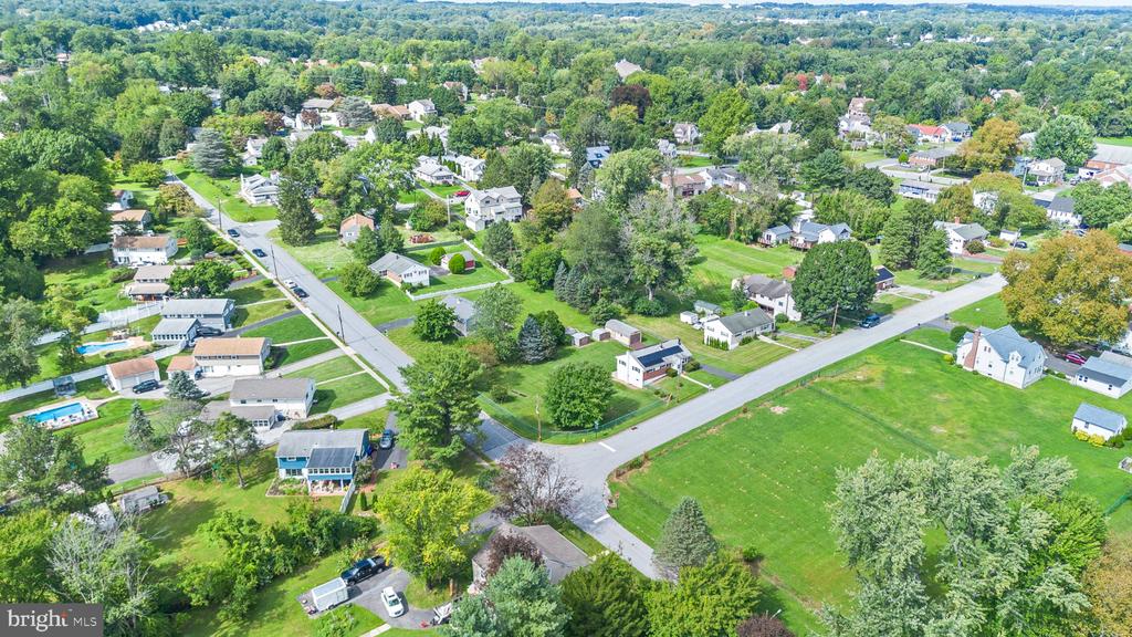 Aerial view of a leafy neighborhood with detached homes, intersecting roads, and an open grassy lot.