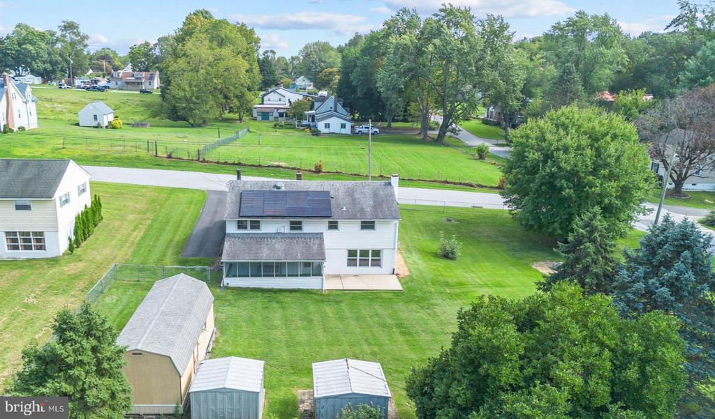 Aerial view of a white two-story house with solar panels, screened porch, sheds, and a broad lawn.