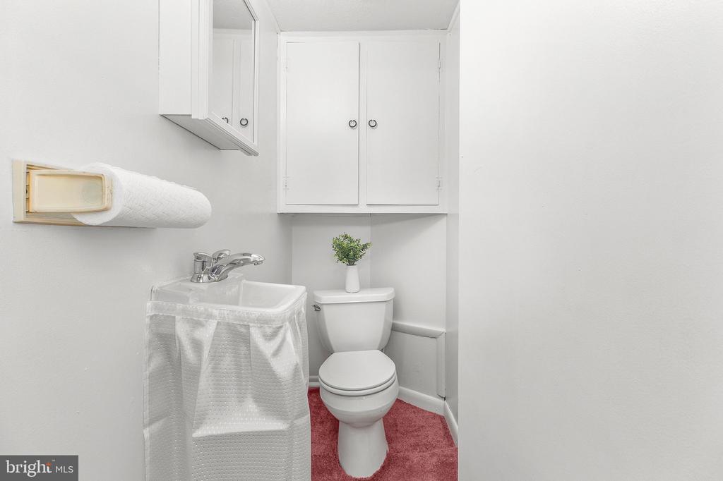 Powder room with a skirted sink, white wall cabinets, and red carpet.