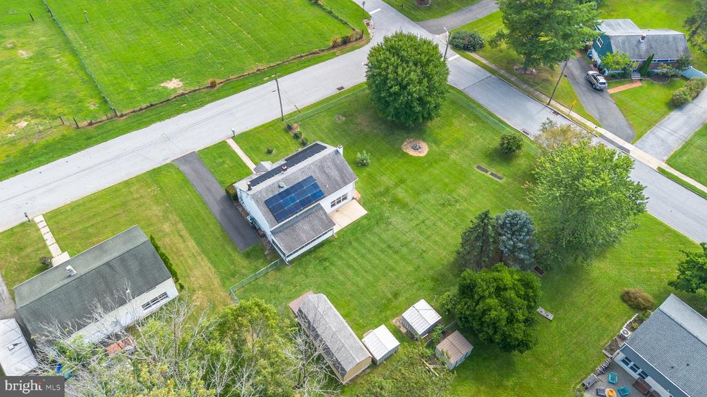 Aerial view of a house with rooftop solar panels and a broad lawn bordered by mature trees.