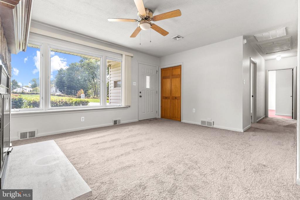 Vacant living room with a large window, ceiling fan, and wooden closet doors.
