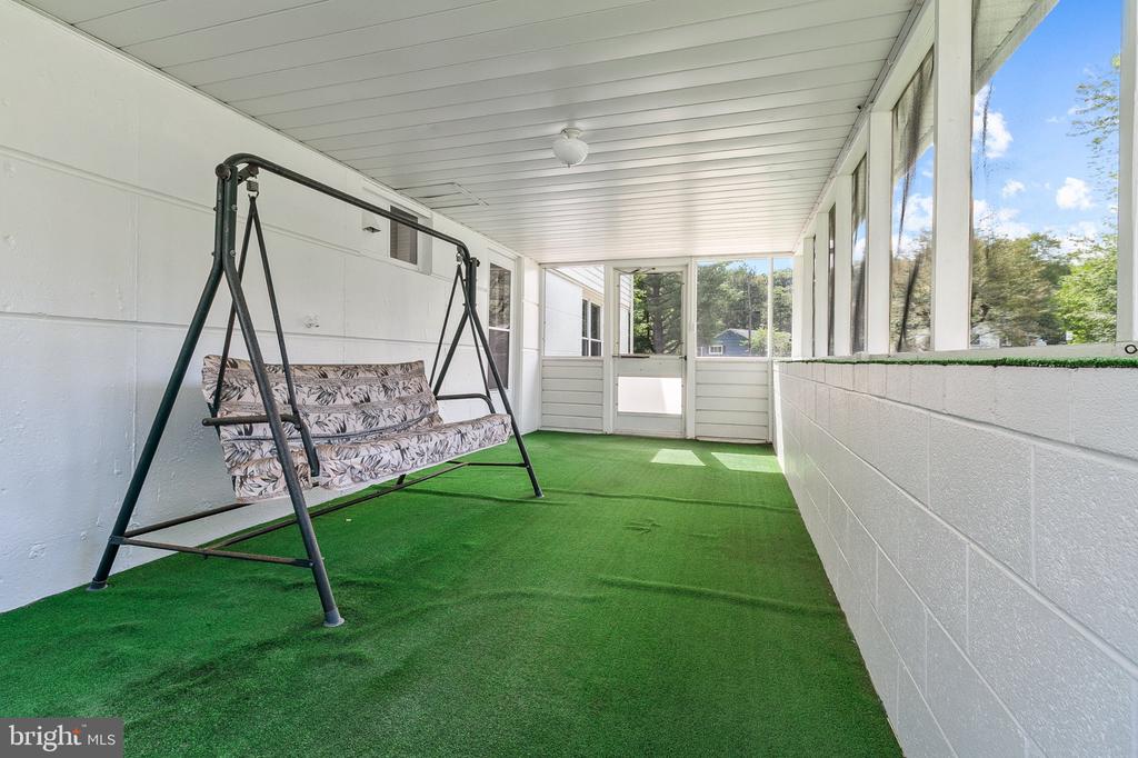 Enclosed porch with green turf flooring, large windows, and a cushioned swing.